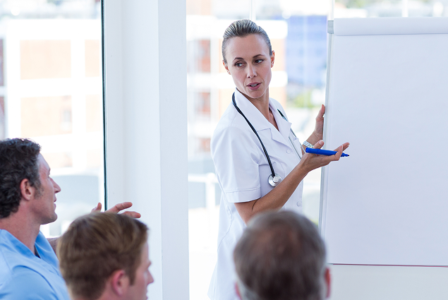 Pflegefachperson steht vor einer Gruppe und erläutert Inhalte an einem Flipchart.