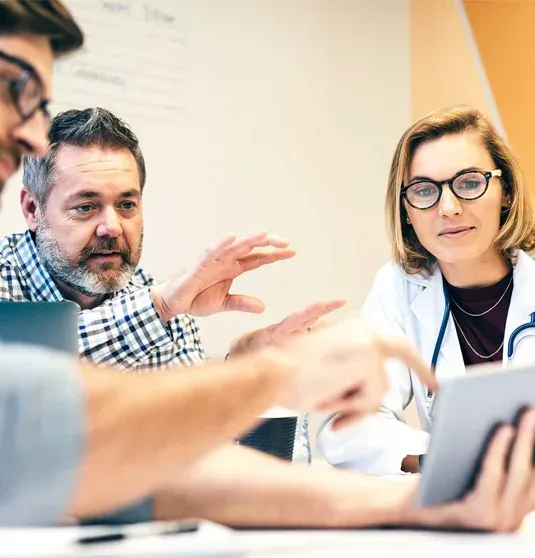 Drei Personen sitzen an einem Tisch und besprechen gemeinsam Inhalte auf einem Tablet.