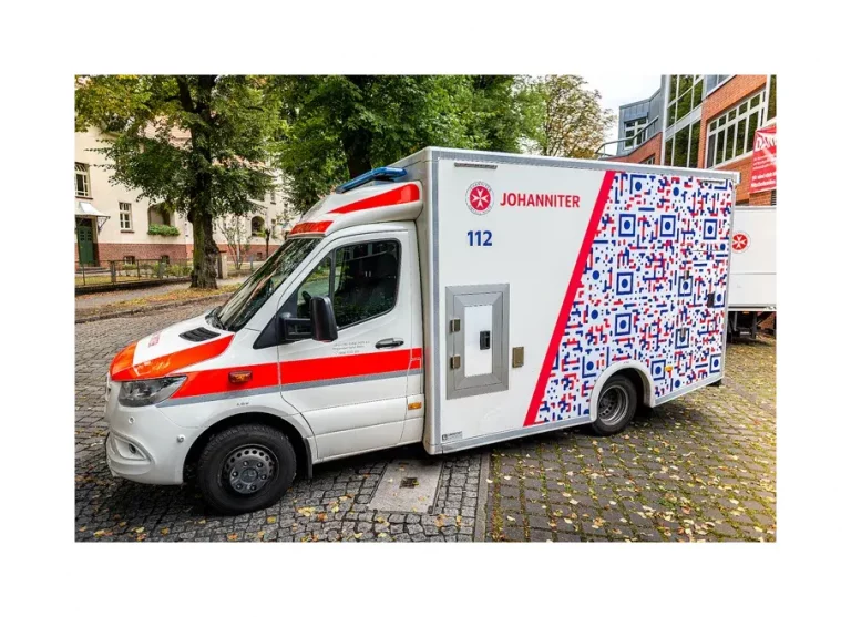 Rettungswagen der Johanniter steht auf einem gepflasterten Gelände vor einem Gebäude.