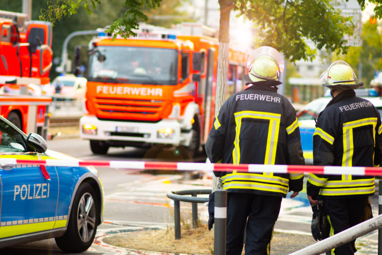 Einsatzkräfte der Feuerwehr und Polizei sichern eine Unfallstelle mit Einsatzfahrzeugen und Absperrband ab.