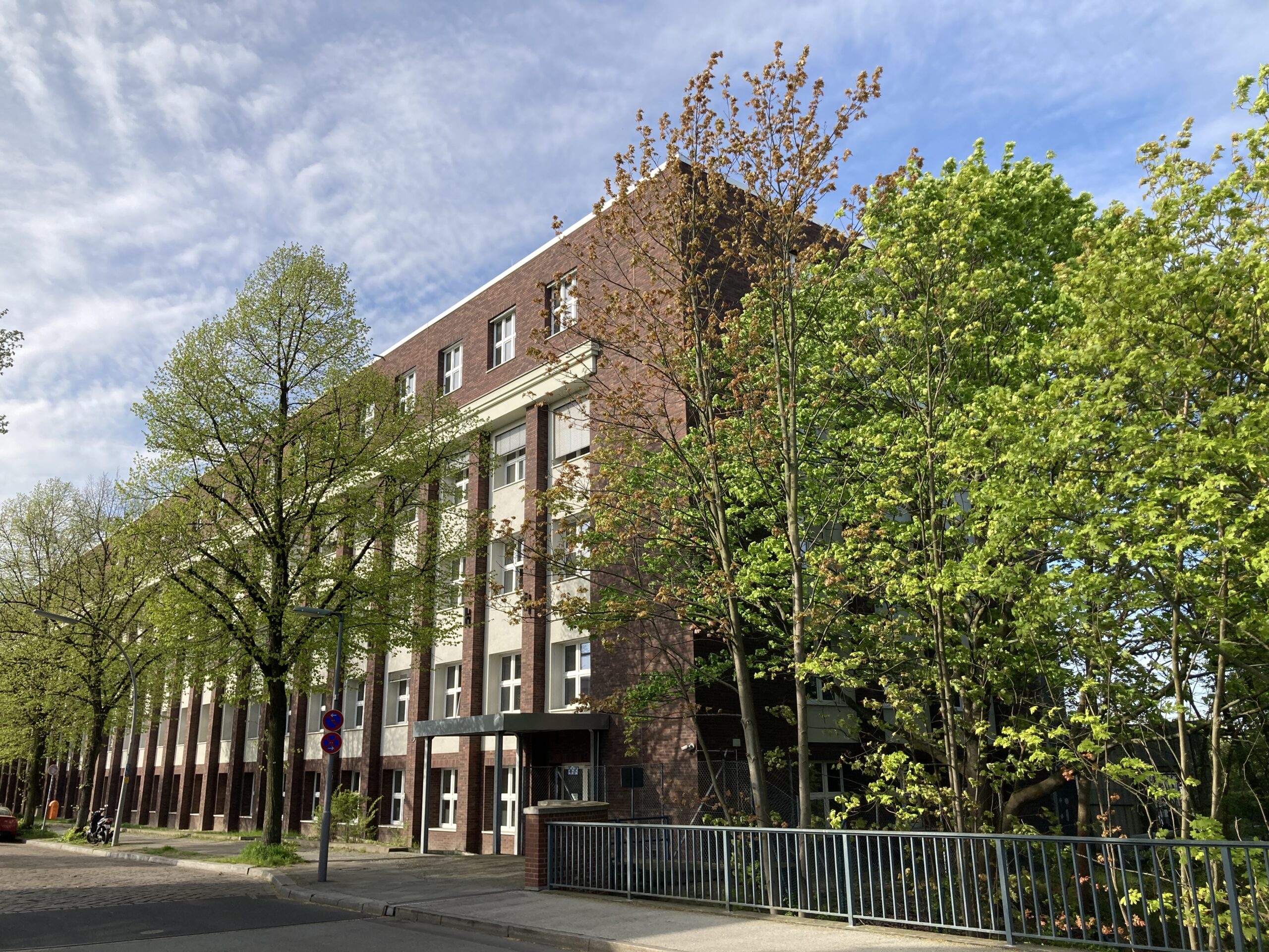 Außenansicht des Gebäudes der Akkon Hochschule für Humanwissenschaften mit umliegenden Bäumen.