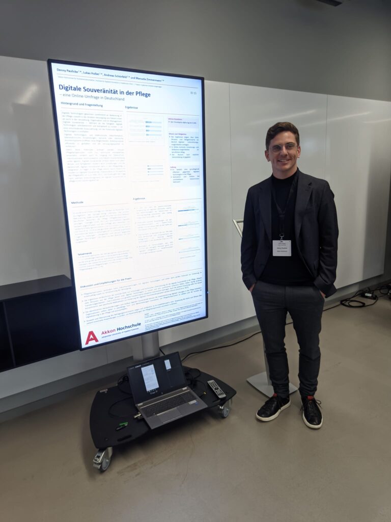 Eine Person steht neben einem großen digitalen Posterdisplay, das Forschungsergebnisse zur digitalen Souveränität in der Pflege zeigt. Vor dem Display steht ein Laptop auf einem rollbaren Stand. Die Szene befindet sich in einem modernen Konferenz- oder Tagungsraum.