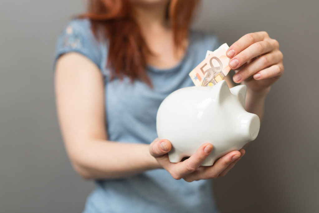 Eine Person hält ein weißes Sparschwein in den Händen und steckt 50-Euro-Scheine hinein, Symbolbild für Sparen oder finanzielle Planung.