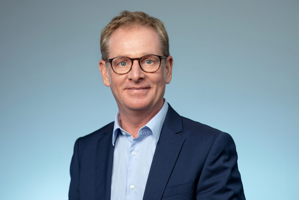 Professionelles Porträtfoto von Prof. Dr. Ansgar Hörtemöller. Er trägt eine Brille, ein hellblaues Hemd und ein dunkles Sakko. Der Hintergrund ist neutral hellblau, der Bildstil sachlich und modern.