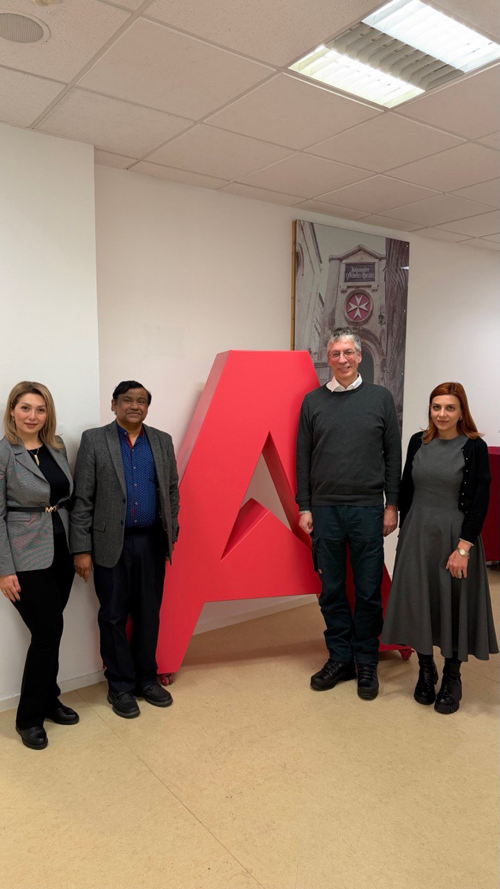 Vier Personen stehen in einem Innenraum der Akkon Hochschule vor einem großen roten Buchstaben „A“. Die Gruppe posiert für ein Erinnerungsfoto im Rahmen eines internationalen Austauschs und symbolisiert die Zusammenarbeit zwischen der Akkon Hochschule und einer internationalen Partnerhochschule.